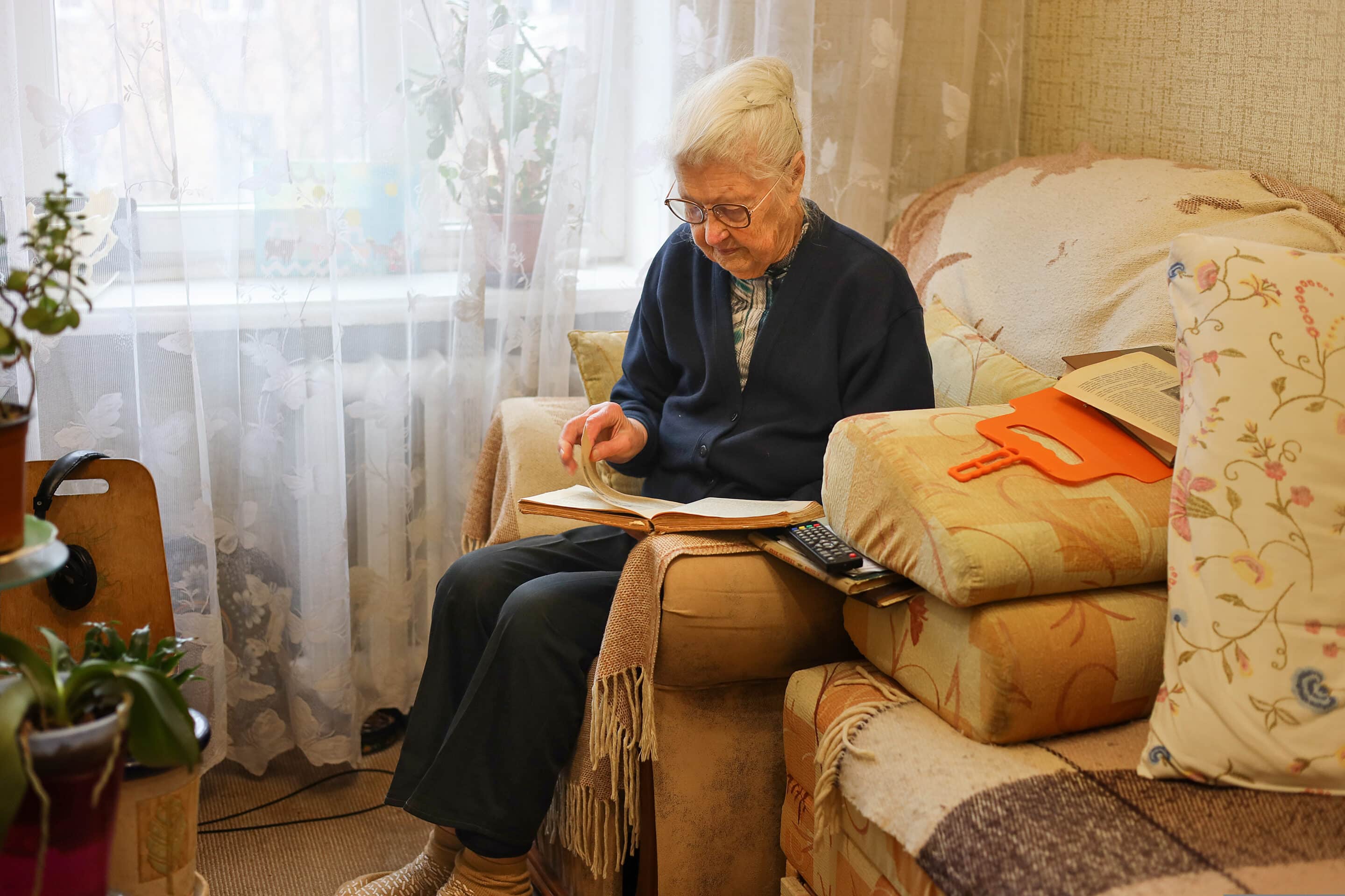 Elderly woman reading a book in a comfortable armchair at home