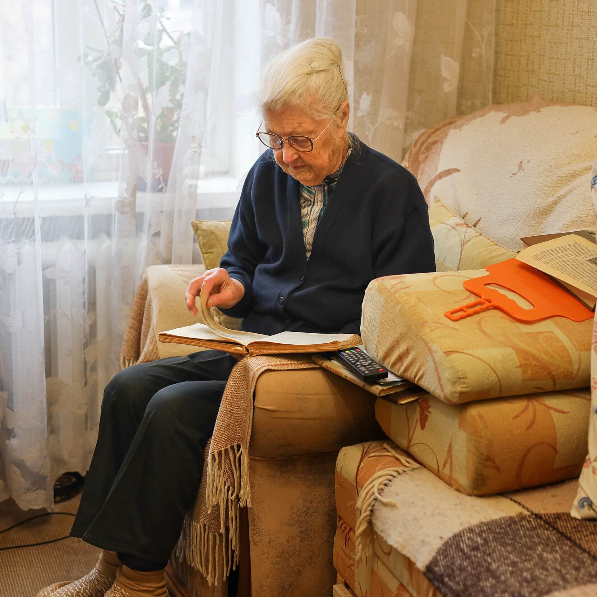 Elderly woman reading a book in a comfortable armchair at home